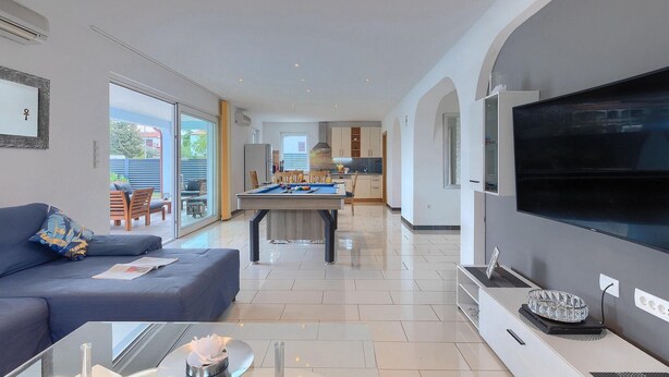 A modern living room with a sofa, a pool table, a flat-screen TV, and a kitchen in the background. - Awesome home in Porec with sauna (Porec)