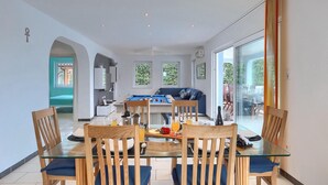 A dining area with a glass table and wooden chairs, a sofa in the background, and a view through a glass door to an outdoor patio. - Awesome home in Porec with sauna (Porec)