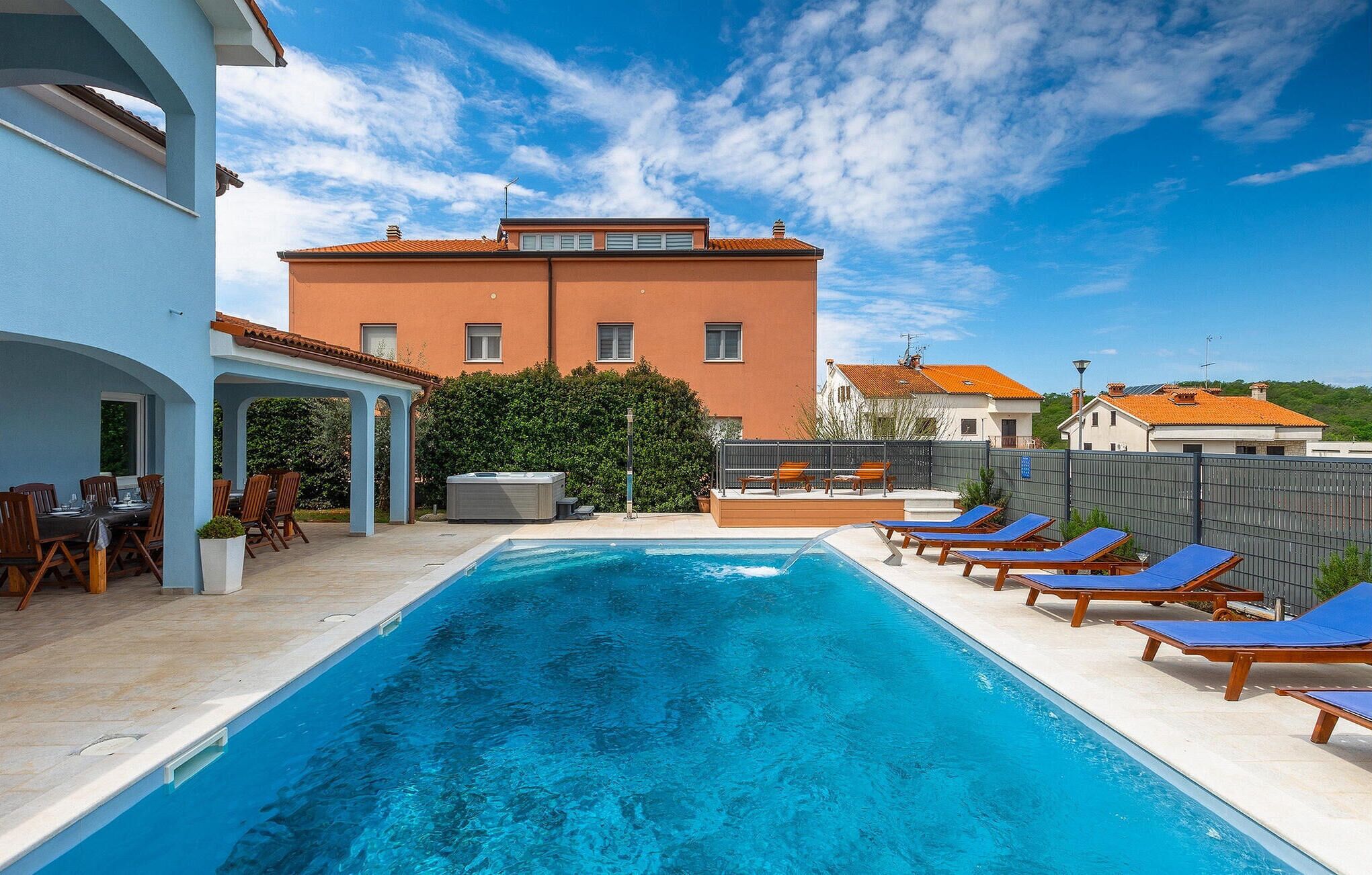 A swimming pool with lounge chairs, a hot tub, and a covered patio area.