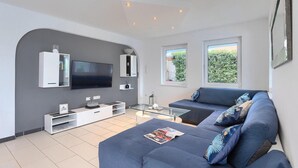 A modern living room with a flat-screen TV, built-in shelving, a glass coffee table, and a blue sofa with decorative pillows. - Awesome home in Porec with sauna (Porec)