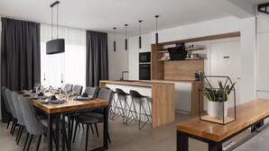 A modern kitchen with a wooden island, black appliances, and a dining area with a long table and chairs.