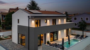 A modern two-story house with a covered outdoor swimming pool, large windows, and a flat roof.