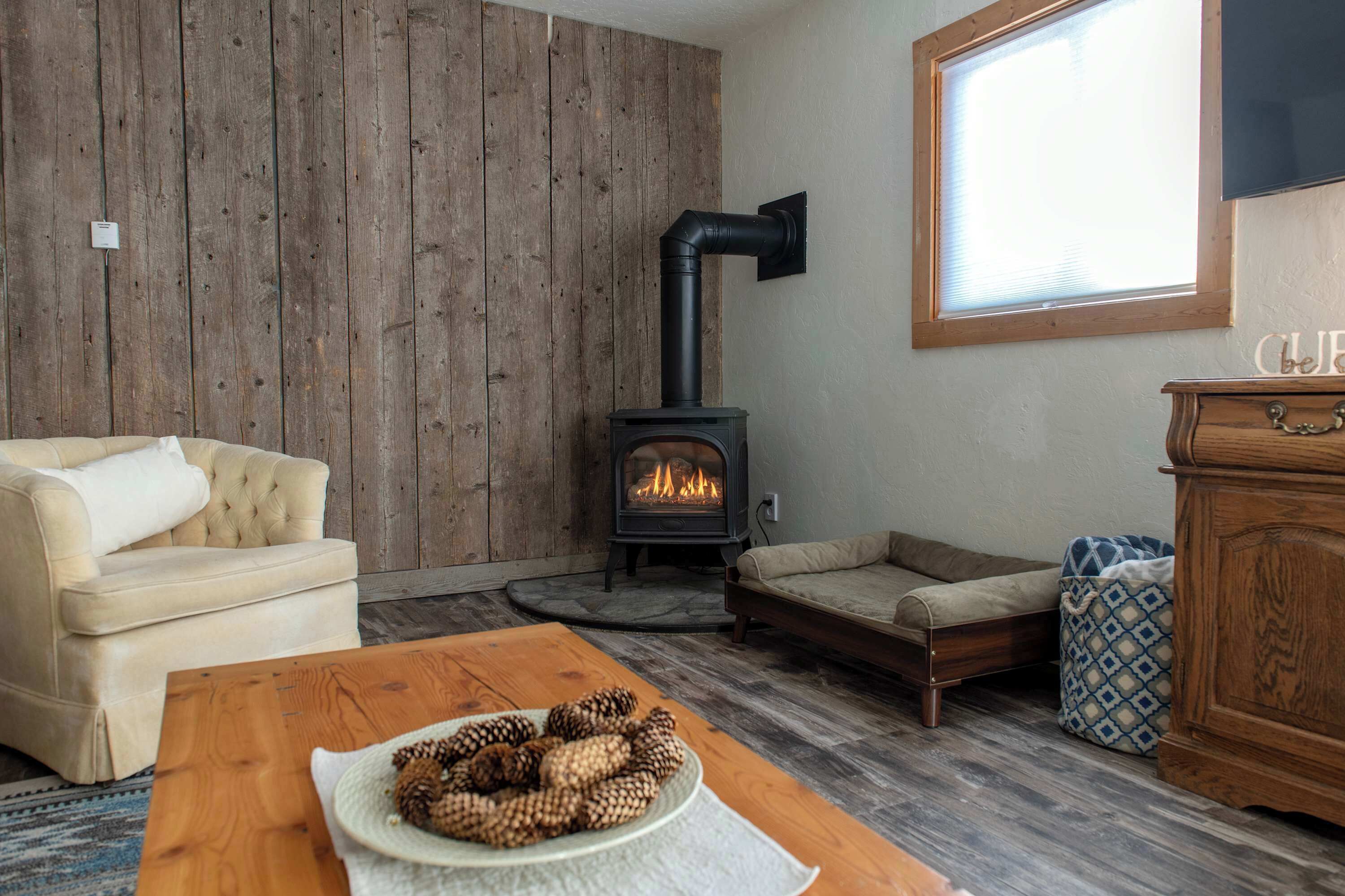 Ein gemütliches Wohnzimmer mit Holzwand, einer Couch, einem Couchtisch mit Kiefernzapfen, einem Kamin und einem Fenster.