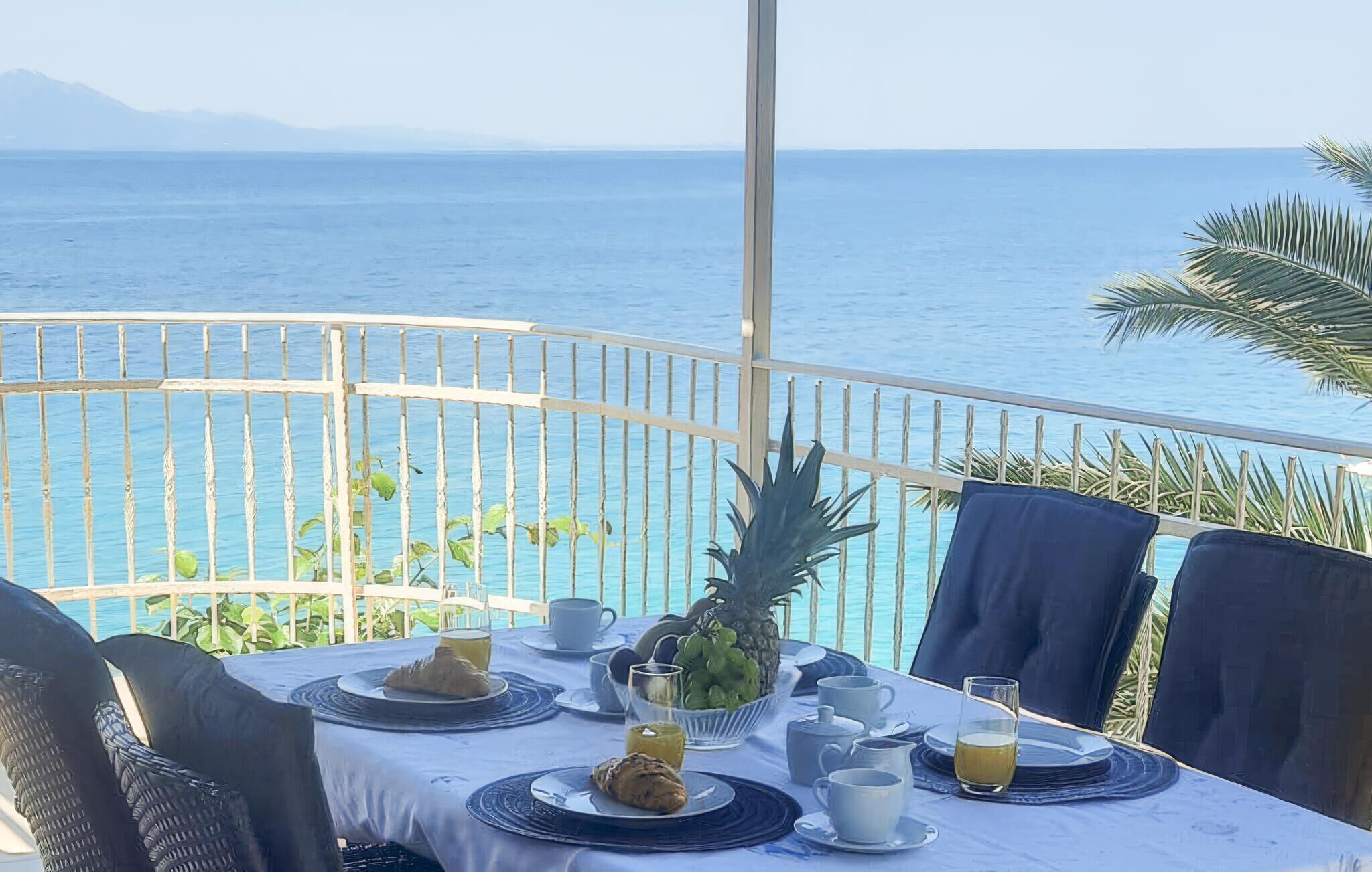 Ett dukat bord för frukost med utsikt över havet, med tallrikar fyllda med mat, koppar och en ananas.