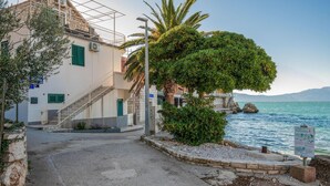A coastal building with a staircase leading to a balcony, a view of the sea, and a signboard by the water. - 2 bedroom cozy apartment in Podaca (Podaca)