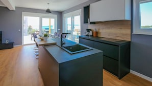 Une cuisine moderne dotée d’un îlot central, d’appareils électroménagers intégrés et offrant une vue sur l’extérieur.