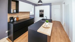 Une cuisine moderne dotée d’un îlot central, de meubles de rangement noirs et d’un plan de travail en bois.