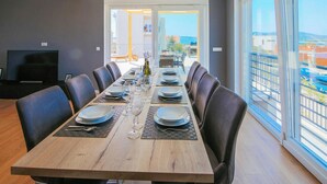 Une salle à manger avec une longue table dressée pour six personnes, un téléviseur et une vue sur la mer grâce à de grandes fenêtres.