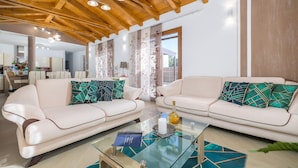 A modern living room with two white sofas, a glass coffee table, and a wooden ceiling.