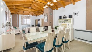A dining area with a glass table and chairs, a sofa, a fireplace, and a clock on the wall.