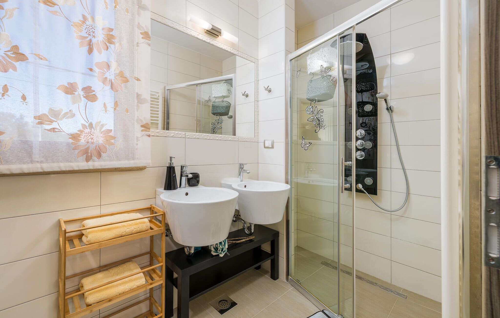A modern bathroom with two sinks, a glass shower enclosure, and a wooden towel rack.