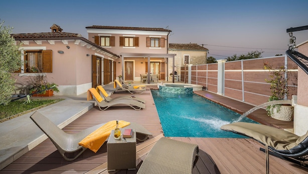 A pool area with lounge chairs and a hot tub, surrounded by a house with a patio.