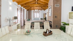 A spacious living room with a high ceiling, a sofa set, a glass coffee table, and a fireplace.