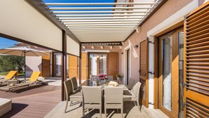 An outdoor patio with a covered seating area, a table with chairs, and a potted plant.