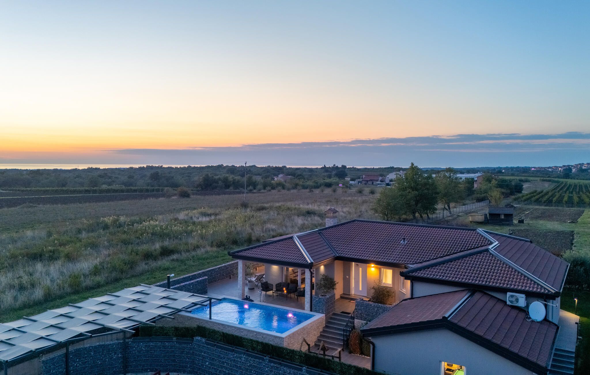 Ein Haus mit Swimmingpool, überdachter Terrasse und Meerblick bei Sonnenuntergang.