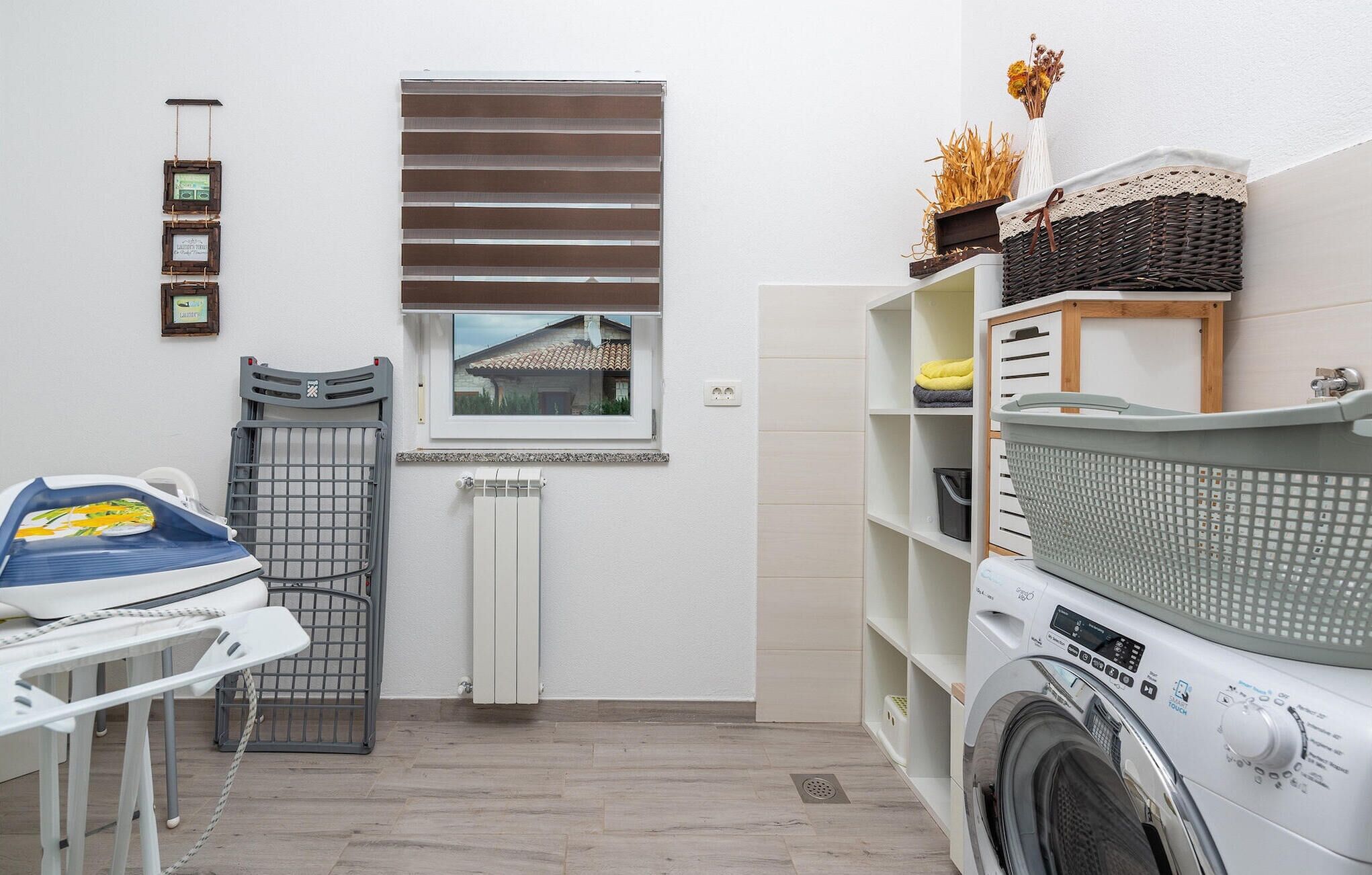 A laundry room with a washing machine, drying rack, and ironing station.