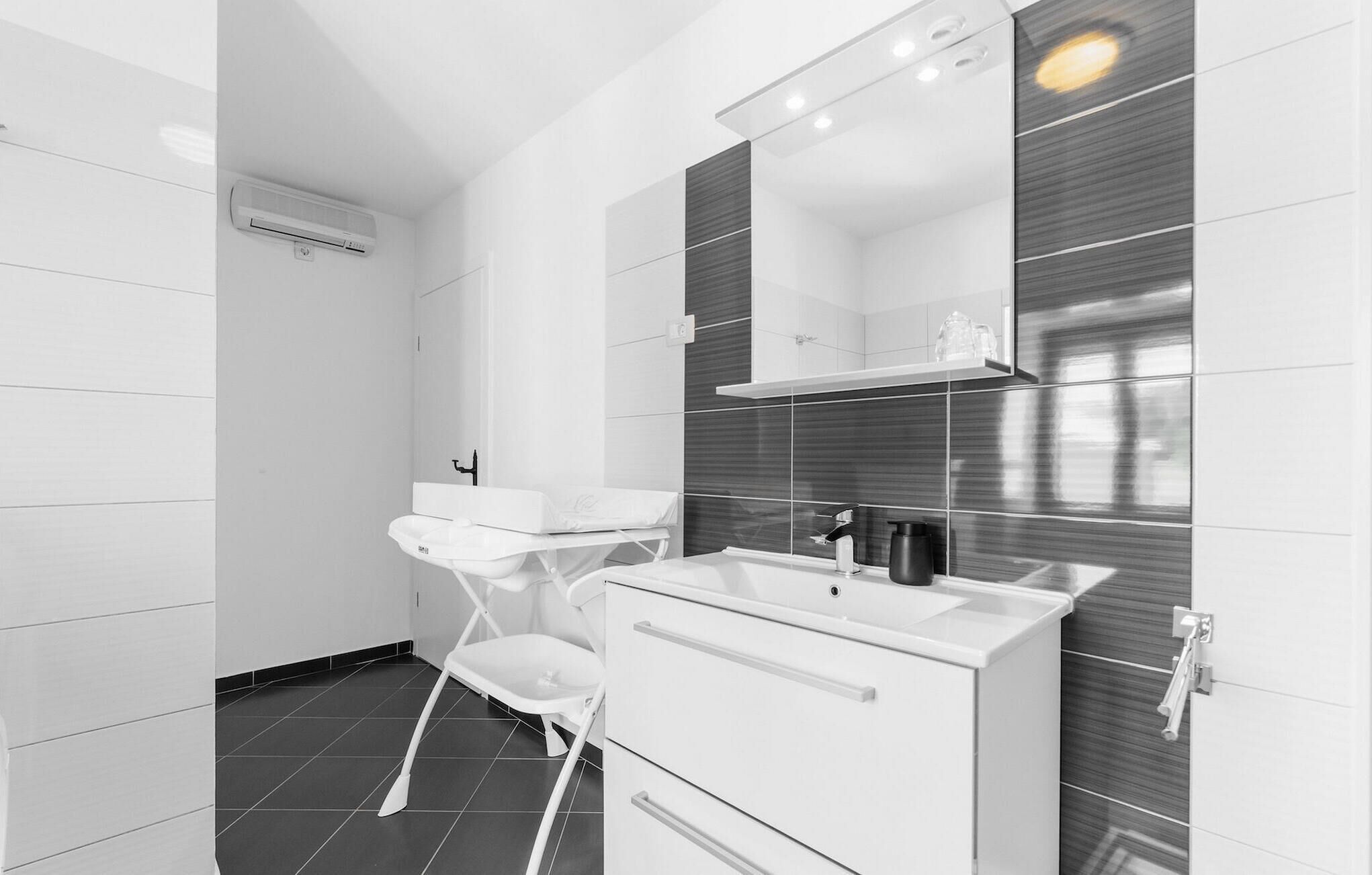 Une salle de bain moderne avec un meuble-lavabo blanc, un miroir, un évier et un espace douche.
