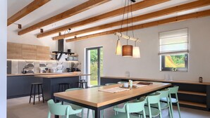 A modern kitchen with wooden beams, a central island, and a dining area with green chairs. - Amazing home in Vizinada (Vizinada)