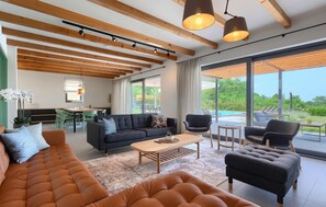 A spacious living area with a large sofa, armchairs, and a coffee table. There is a dining area with chairs and a table, and a view of a swimming pool through large windows. - Amazing home in Vizinada (Vizinada)