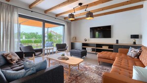 A modern living room with a large window, a flat-screen TV, and a cozy seating area. - Amazing home in Vizinada (Vizinada)