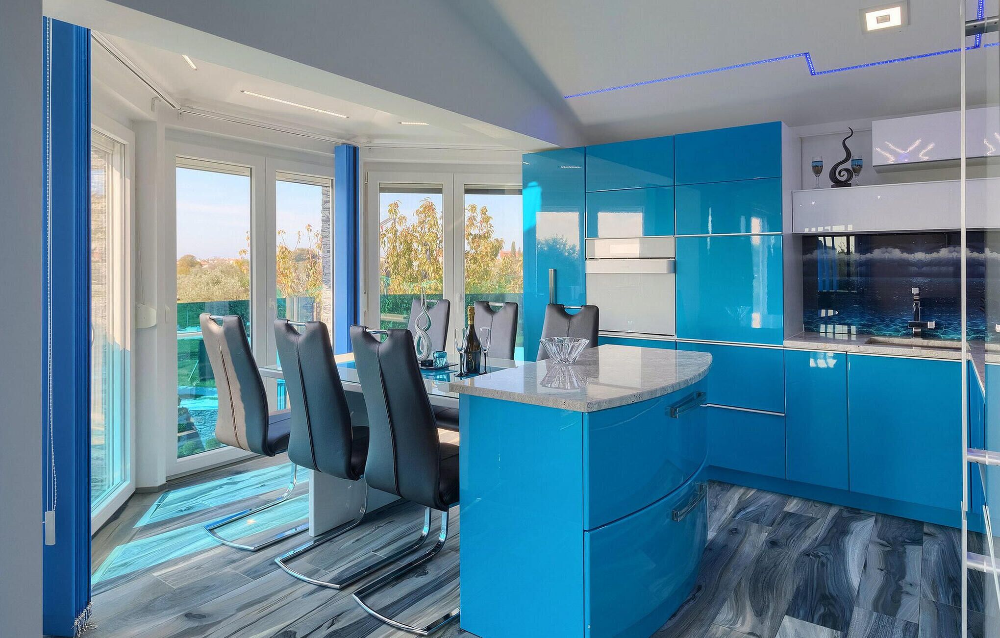 A modern kitchen with blue cabinets, a dining area with chairs, and a view of the outdoors.