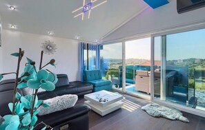 Un salon moderne avec un canapé noir, un fauteuil bleu et une table basse blanche. Une grande fenêtre offre une vue sur une piscine et un espace verdoyant.