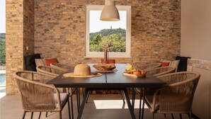 A dining area with a brick wall, wicker chairs, a dark table, and a hanging light fixture. - Amazing home in Labin - Rabac (Labin - Rabac)