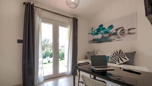 Ein modernes Wohnzimmer mit Glastisch, weißen Stühlen, einer Couch mit gemusterten Kissen, einem Laptop und einem Bild von Delfinen an der Wand.