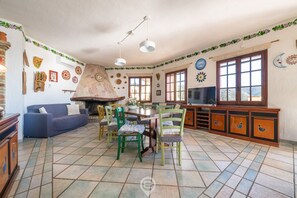 A spacious living room with a fireplace, a dining area with chairs and a table, and a television on the right.