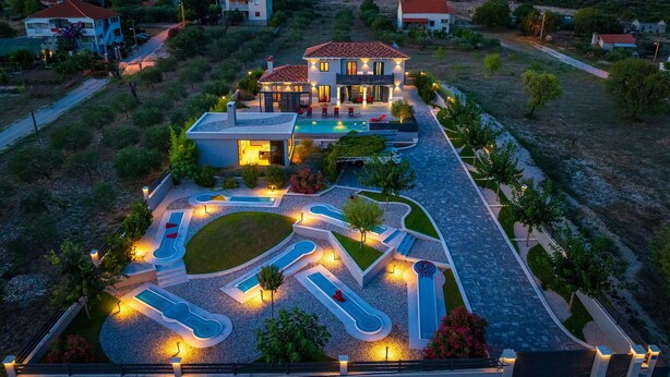 Una casa moderna amb piscina, diverses tobogans aquàtics i un jardí ben cuidat.