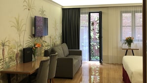 A modern hotel room with a sofa, a dining table with chairs, a TV mounted on the wall, and a bed with a red bedspread. - Chasse Residency Hotel (Amsterdam)