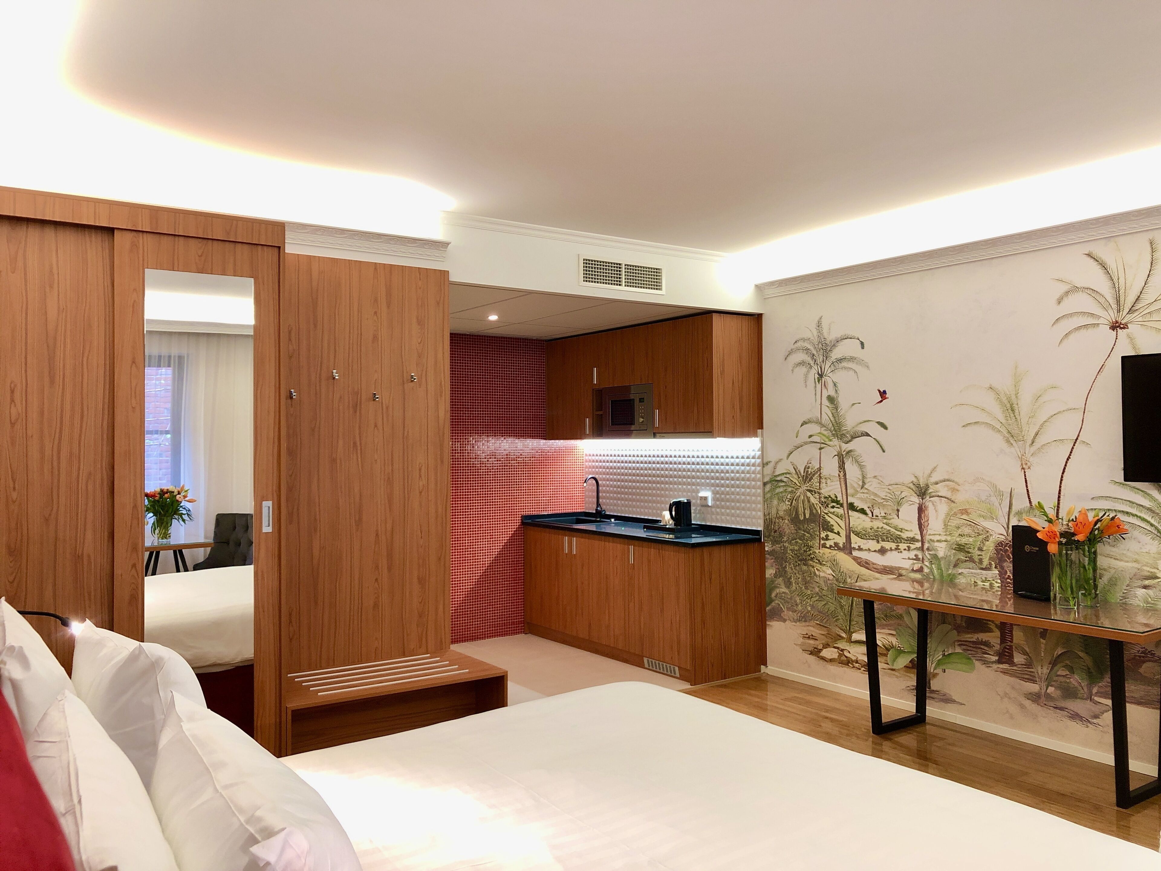 A hotel room with a bed, a small kitchenette, a dining table, and a mural of palm trees.
