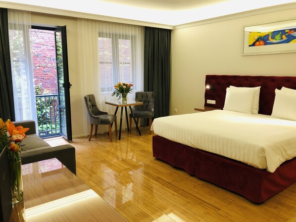 Habitación de hotel con una cama grande, una pequeña mesa con sillas, un florero y vistas a un edificio de ladrillo a través de una ventana.