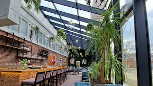 A restaurant with a brick wall, bar area, hanging plants, and outdoor seating. - Chasse Residency Hotel (Amsterdam)