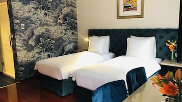 A hotel room with two beds, a dark green headboard, a mural on the wall, and a framed picture above the bed.