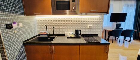 Cocina compacta con microondas, lavabo y una pequeña zona de comedor con sillas.