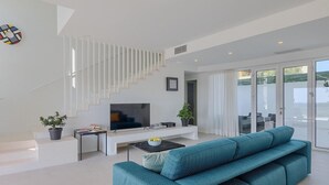 A modern living room with a teal sofa, a flat-screen TV, a staircase, and a balcony with outdoor furniture. - Stunning home in Porec (Porec)