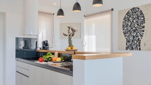 A modern kitchen with white cabinets, a black countertop, and a wooden island. There are three pendant lights, a coffee machine, and a fruit bowl on the counter. - Stunning home in Porec (Porec)