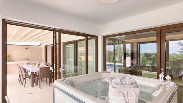 A modern bathroom with a large bathtub, glass doors leading to an outdoor dining area, and a view of the countryside. - Amazing home in Gracisce (Gracisce)