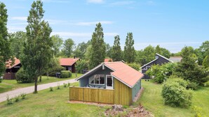 Une petite cabane en bois avec un toit rouge, entourée d’une pelouse bien entretenue et d’arbres.