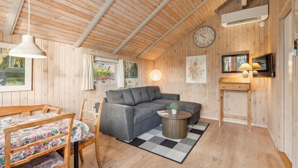 L’intérieur chaleureux d’un chalet avec un canapé, une table à manger et des chaises, une petite table basse ronde et une horloge au mur.