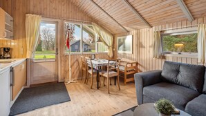 L’intérieur chaleureux d’un chalet avec des murs en bois, un coin repas comprenant une table et des chaises, un canapé et une cuisine équipée d’une machine à café.