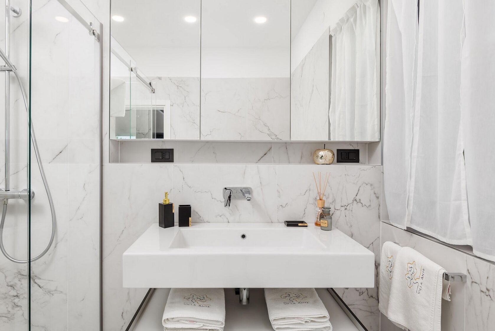 A modern bathroom with a large white sink, a glass shower enclosure, and a marble backsplash.