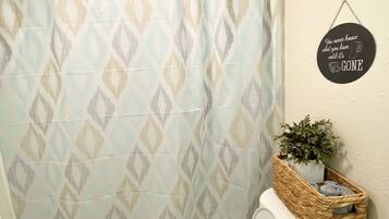 A bathroom with a patterned shower curtain, a toilet, a wicker basket with a plant, and a motivational quote on the wall.
