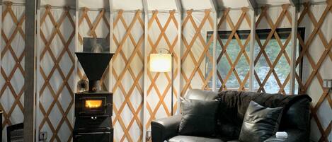 Een gezellig interieur van een tent, met een bank, een klein tafeltje, een lamp en een houtkachel.