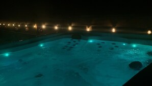 Vista nocturna de un área de jacuzzi con piscina, rodeada de luces uniformemente espaciadas.