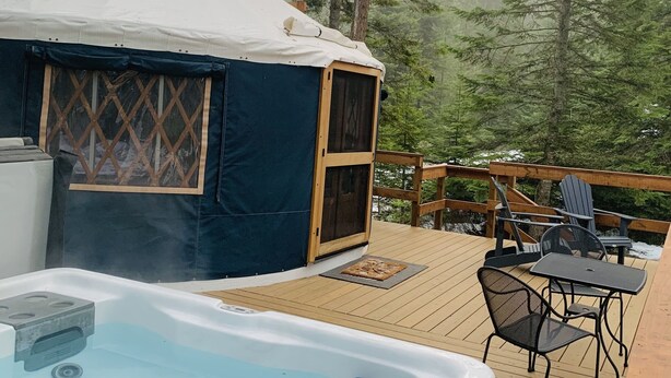 Una yurta con jacuzzi en una terraza de madera rodeada de árboles.