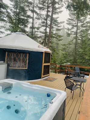 Eine Jurte mit Whirlpool auf einer Holzterrasse, umgeben von Bäumen.