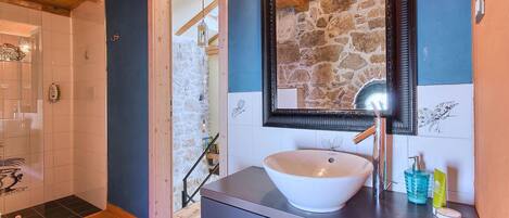 A bathroom with a white sink, a mirror, and a stone wall.
