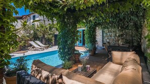 Un área junto a la piscina con terraza de madera, sillas de descanso y un espacio de estar cubierto con cojines.